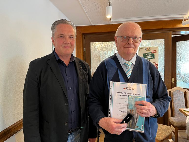 Zwei Herren in Anzügen halten ein Buch und lächeln in die Kamera.